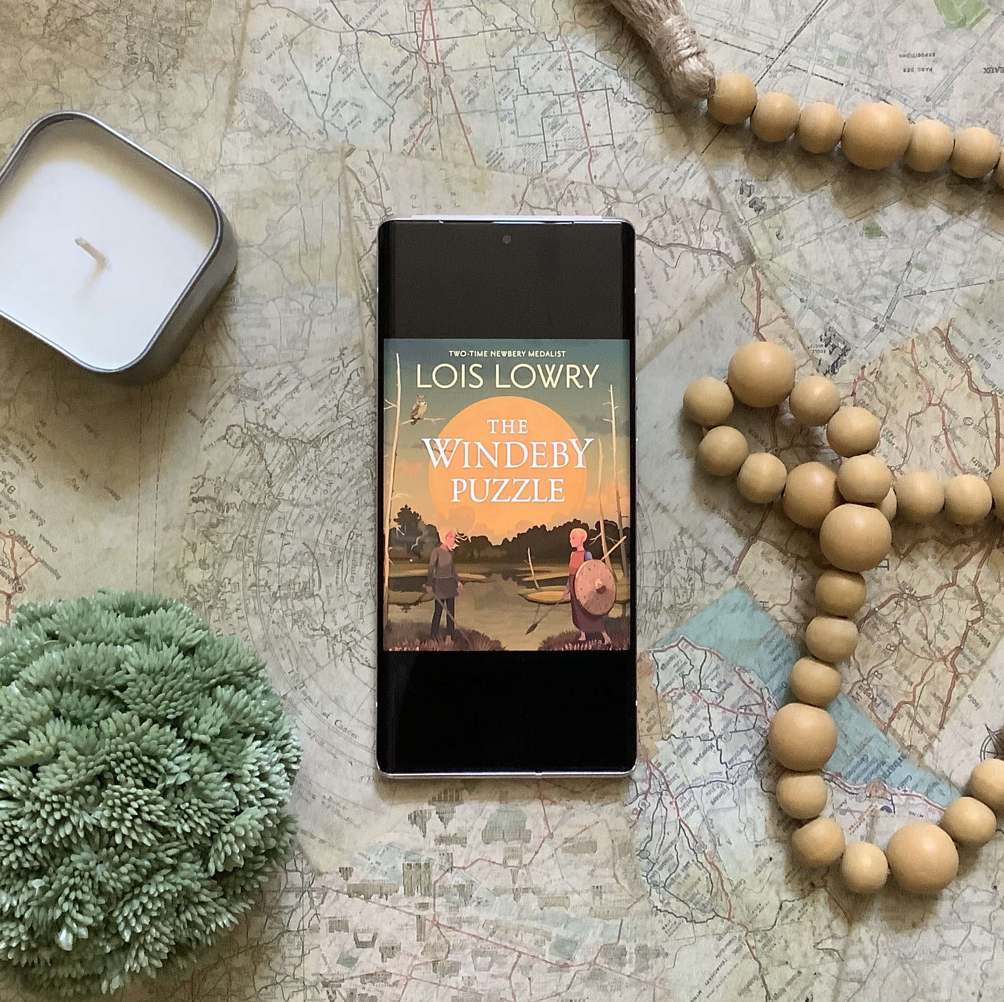 The Windeby Puzzle by Lois Lowry. Ebook cover on a phone with other decorations. A YA historical fiction.